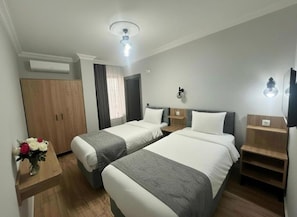 A hotel room with two beds, a wooden wardrobe, a small table with a vase of flowers, and a ceiling fan. - Avka Palace Hotel (Edirne)
