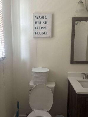 Ein Badezimmer mit Toilette, einem weißen Waschbecken und einem an der Wand befestigten Schild mit der Aufschrift 'WASH. BRUSH. FLOSS. FLUSH.'