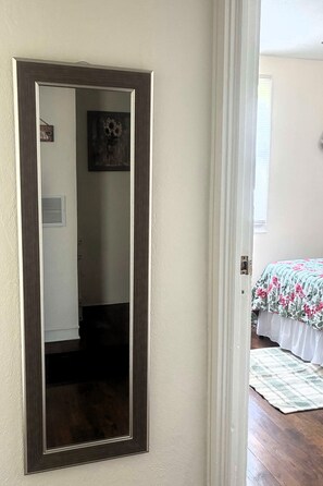 Ein Zimmer mit einem großen Spiegel, einem Bett mit Blumenmuster und einem Fenster mit Jalousien.