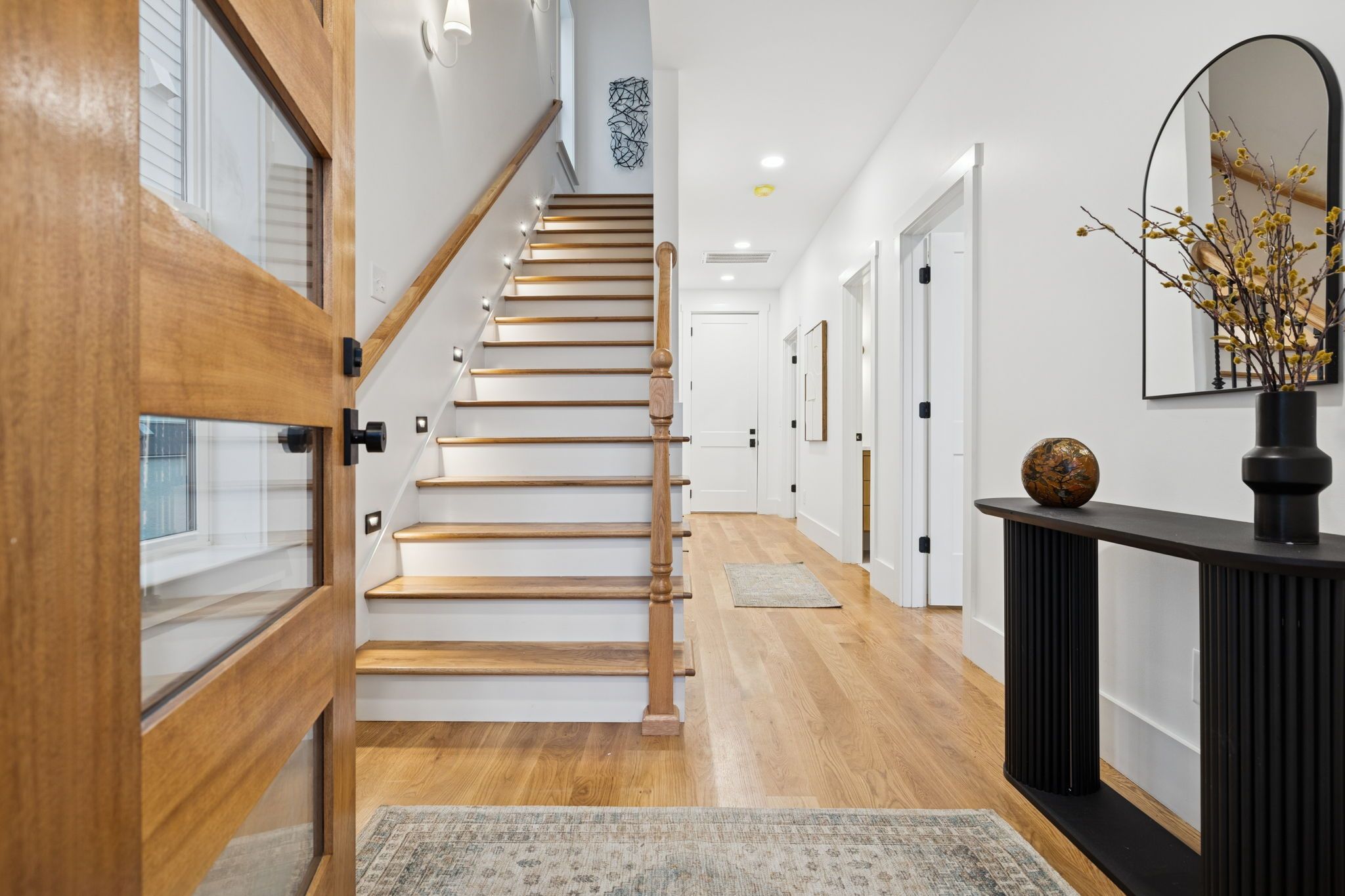 A staircase with wooden steps and a handrail, leading to a room with a door and a wall-mounted mirror.