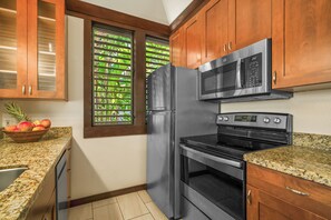 A kitchen with stainless steel appliances, wooden cabinets, a window with blinds, and a fruit bowl on the counter. - Kiahuna 115 - Ground Floor - Corner Unit - Two ACs (Koloa)