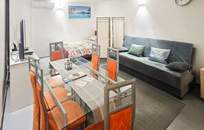 A compact hotel room with a bed, a sofa, a dining table with chairs, a small desk with a computer, and a clock on the wall. - 1 bedroom pet friendly home in Delekovec (Delekovec)