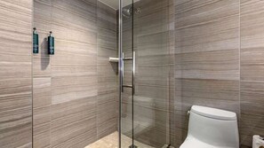 A modern bathroom with a glass shower enclosure, a white toilet, and a tiled wall. - Elegant Georgetown Retreat | Hilton 1BR Suite | Walk to Shops & Dining (Washington)