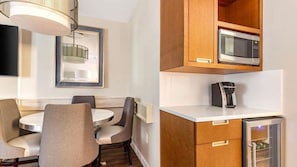 Una cocina compacta equipada con microondas, cafetera y refrigerador. Hay un comedor con una mesa redonda y sillas.
