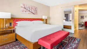 A hotel room with a large bed, a red bench, a wooden nightstand, and a red patterned rug. - Elegant Georgetown Retreat | Hilton 1BR Suite | Walk to Shops & Dining (Washington)