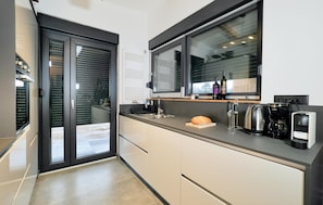 A modern kitchen with a large window, a coffee maker, and a bread loaf on the counter. - Cozy home in Lovinac with sauna (Lovinac)