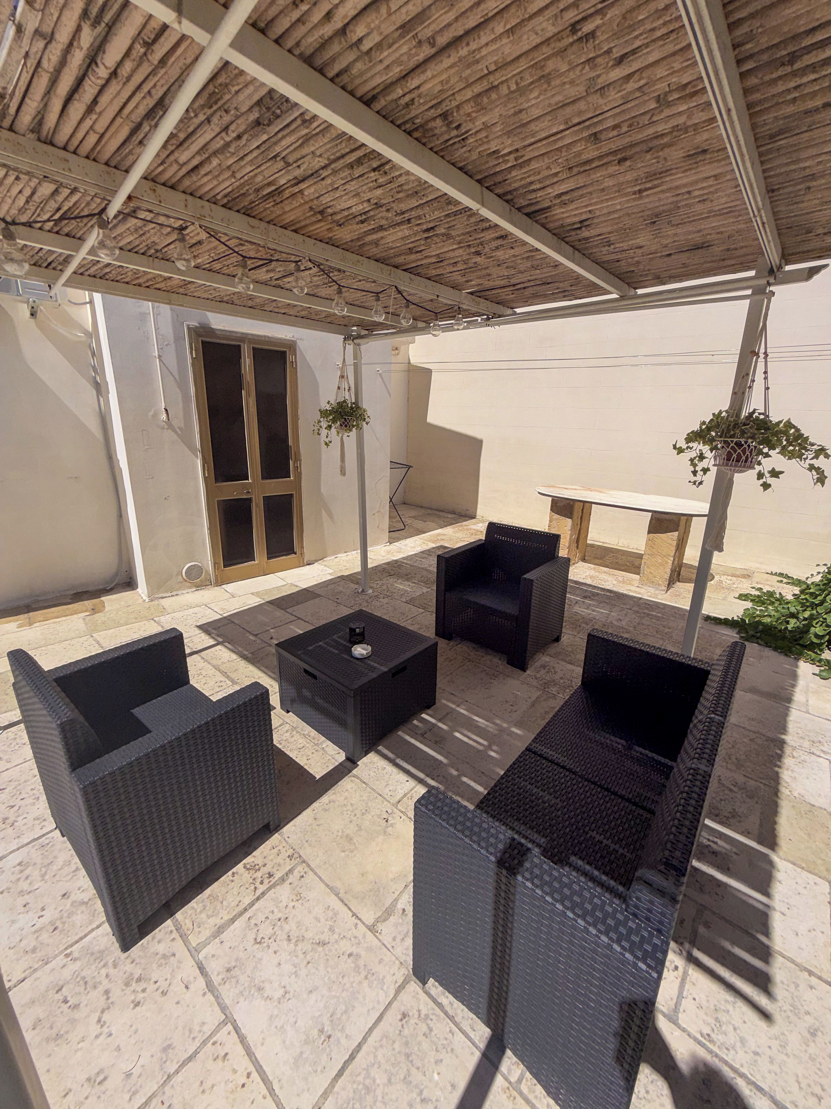 Une terrasse extérieure aménagée avec des meubles en osier, une table et des plantes suspendues.
