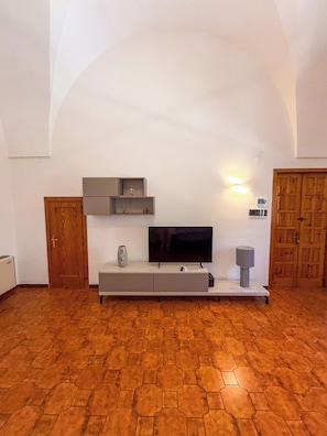 Ein Zimmer mit einem Fernseher auf einem weißen Schrank, einer Holztür und einem gemusterten Boden.