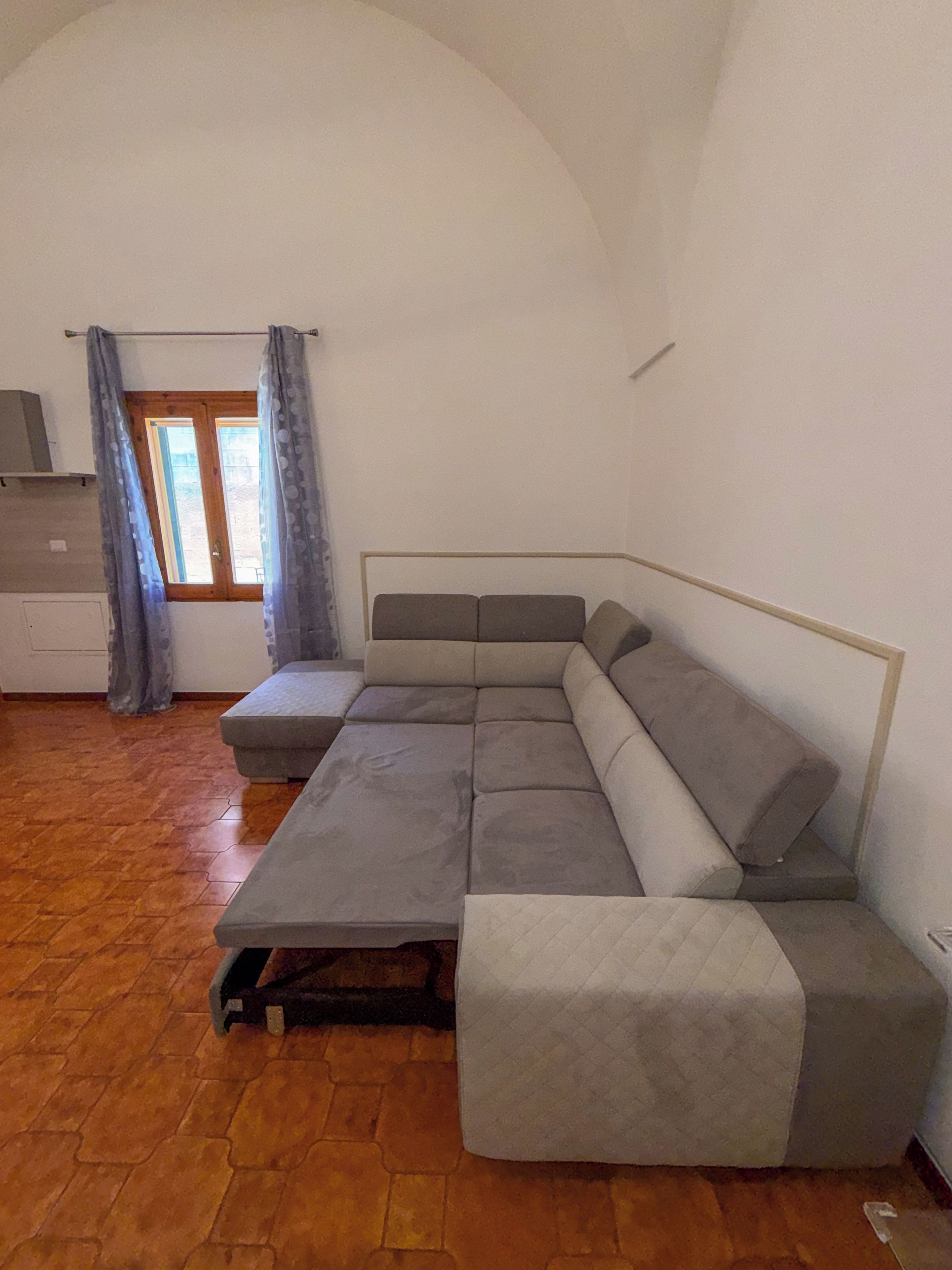 A modern living room with a sectional sofa, a small table, and a window with curtains.