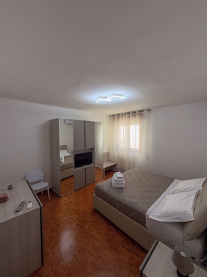 Habitación de hotel con cama, escritorio, televisor y espejo.