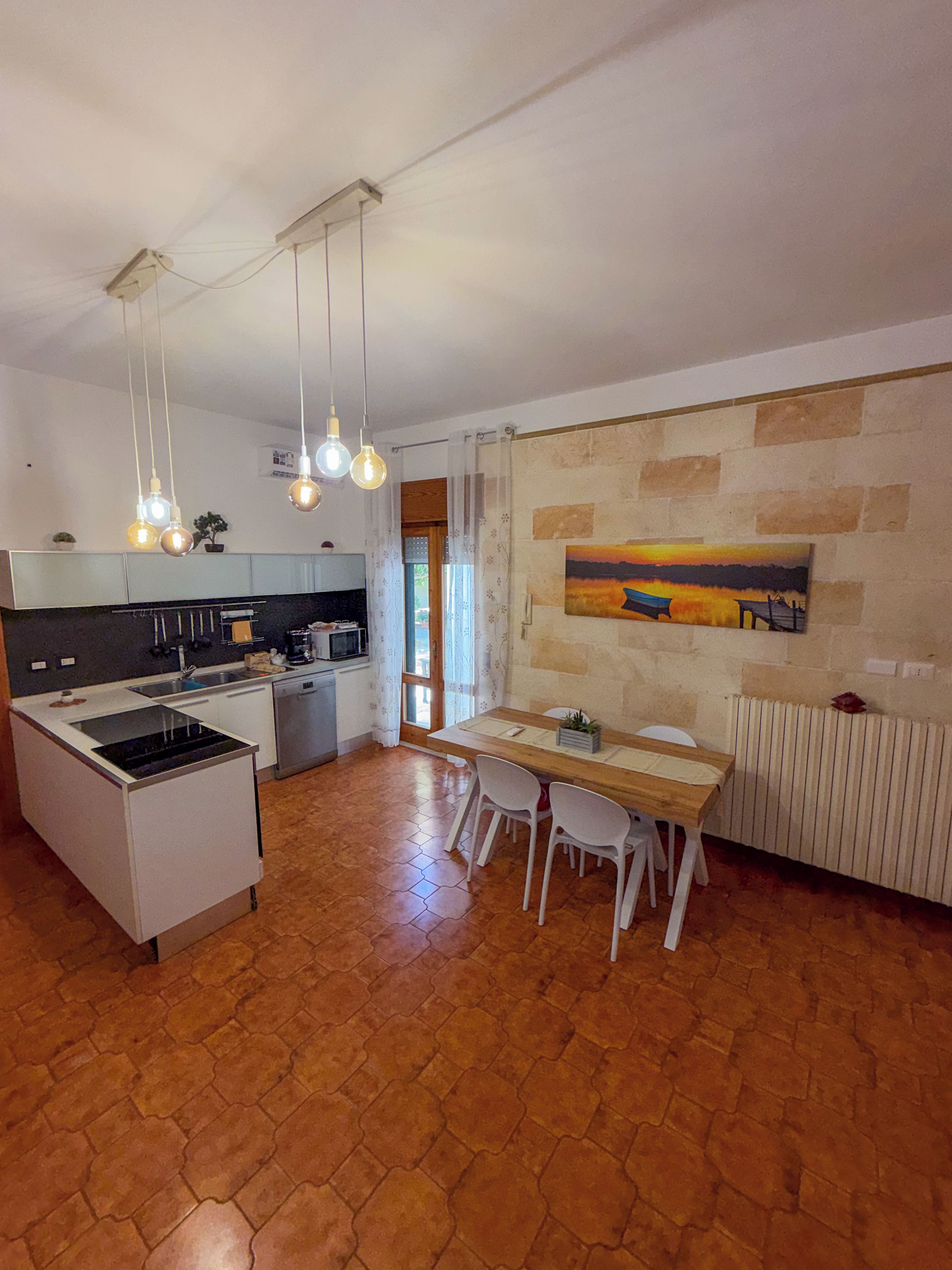 Een moderne keuken met een centraal eiland, hangende lampen en een eethoek met een tafel en stoelen.