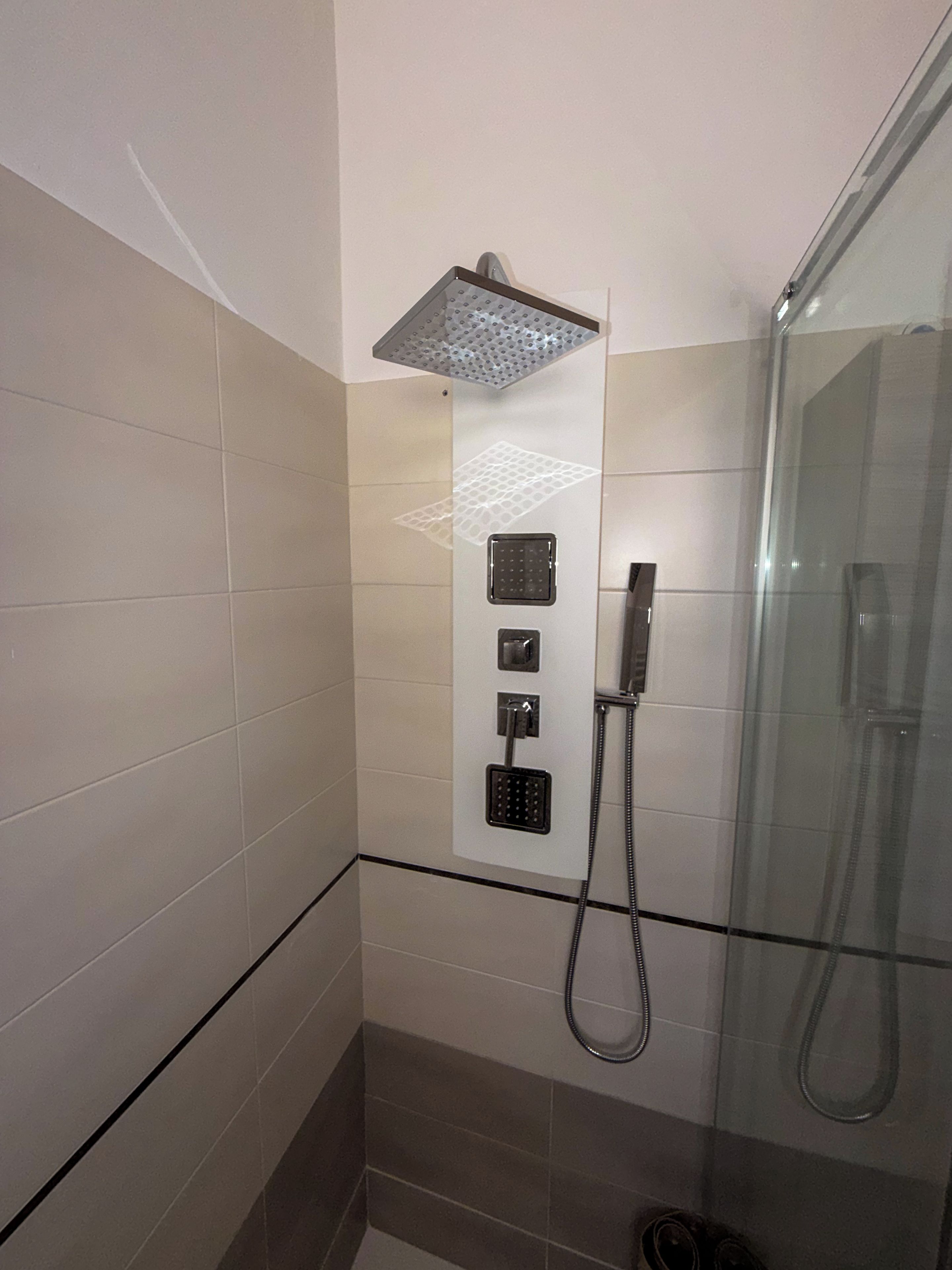 Un espace douche doté d’une paroi en verre, d’un pommeau de douche à main et d’un panneau de commande fixé au mur.
