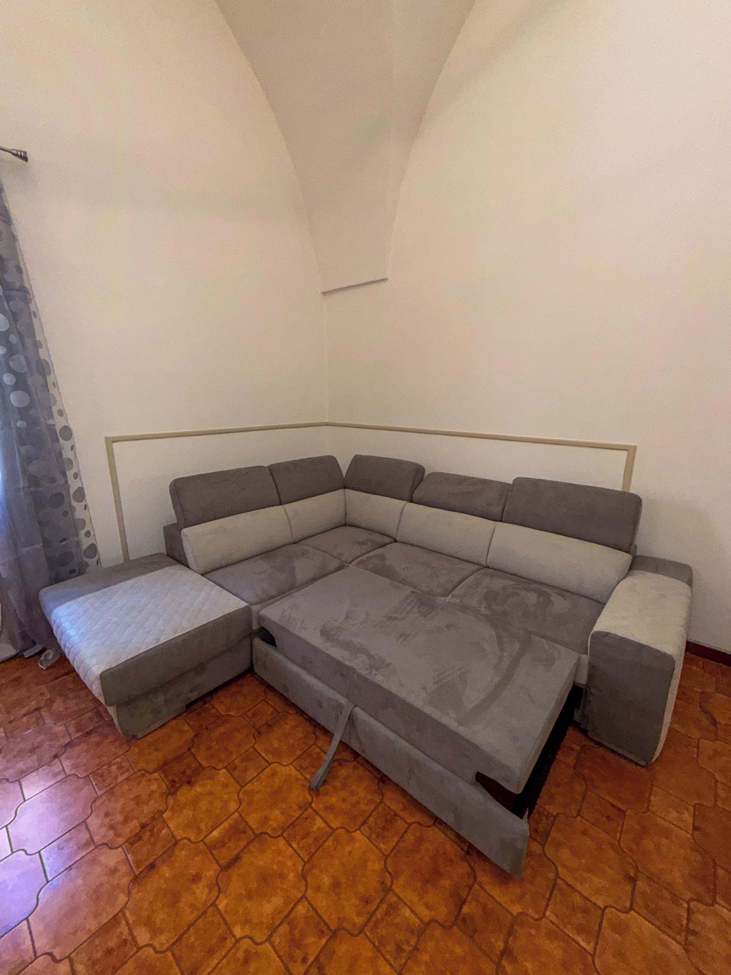 Ein Ecksofa mit Schlafsofa in einem Zimmer mit Fliesenboden und einer schlichten weißen Wand.