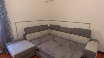 Ein Ecksofa mit Schlafsofa in einem Zimmer mit Fliesenboden und einer schlichten weißen Wand.