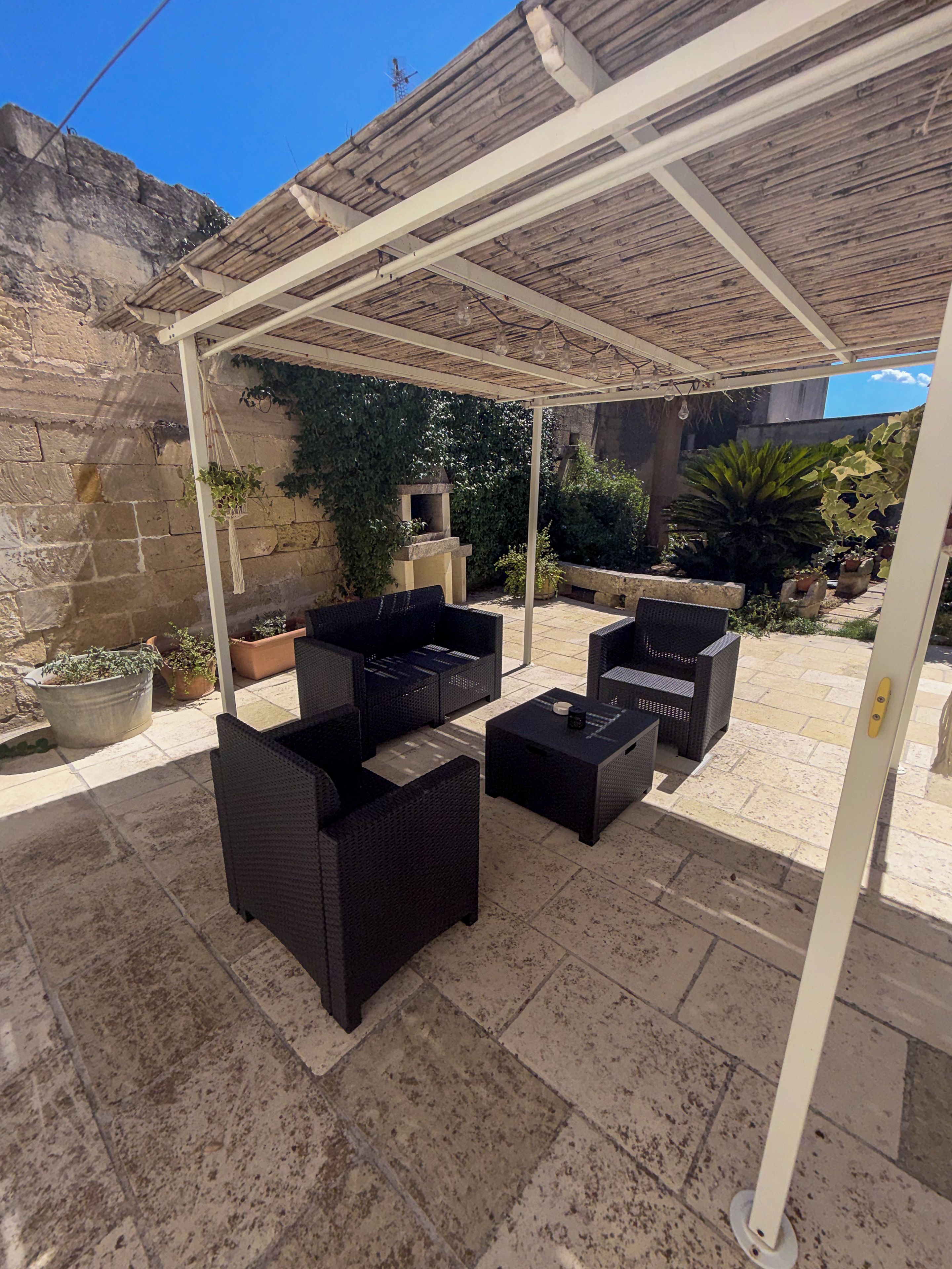 Un espace extérieur aménagé en terrasse, avec une pergola, des meubles en osier et des plantes en pot.