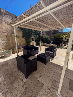 Un patio exterior con pérgola, mobiliario de mimbre y plantas en macetas.