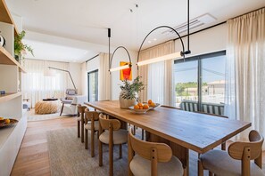 A modern dining area with a wooden table, chairs, and a bowl of fruit. - Villa Nostra w/ Pool, Gym & Tennis Court (Albufeira)