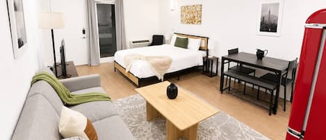 Moderni hotellihuone, jossa on sänky, sohva, ruokapöytä ja punainen jääkaappi.