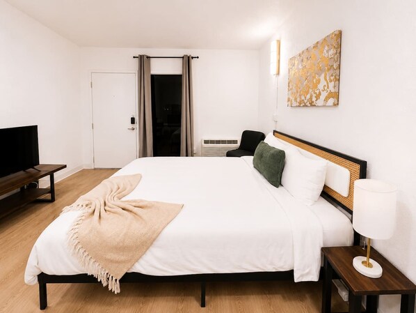 A hotel room with a bed, bedside tables, a lamp, a television, and a painting on the wall. - Sleepover | Splendid Studio + Gym - Austin TX (Austin)