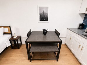 Une cuisine moderne avec une table en bois foncé, des armoires blanches et une photographie représentant un paysage urbain accrochée au mur.