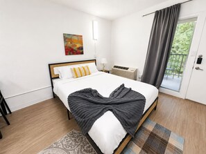 Une chambre d’hôtel avec un lit, un tableau au mur, une fenêtre avec des rideaux et une porte.