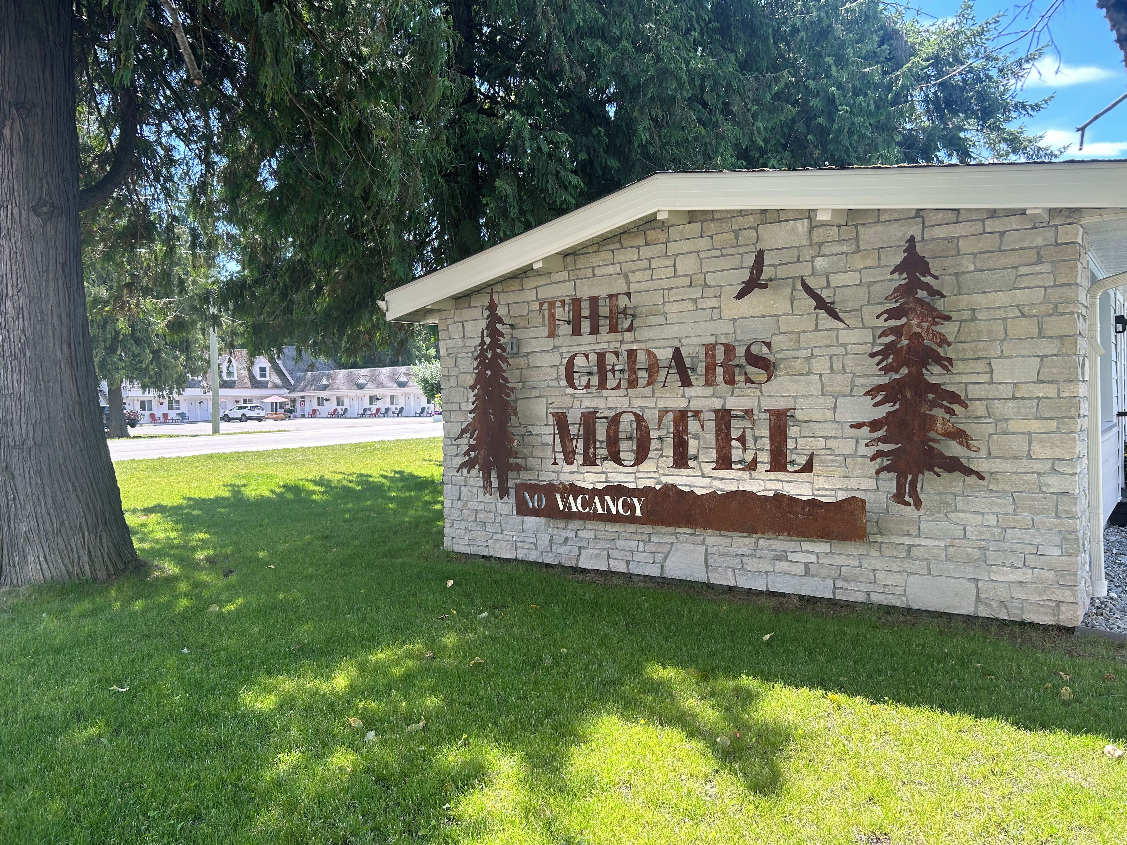 A motel sign with a tree silhouette and the words 'The Cedars Motel' and 'No Vacancy'.