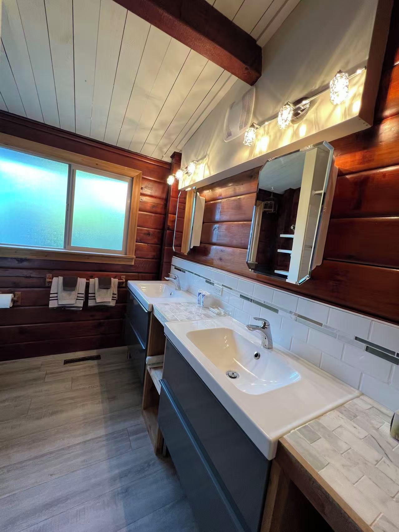 Une salle de bain moderne avec des murs en bois, un grand miroir et un double vasque.