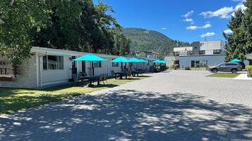 A row of mobile homes with outdoor seating and umbrellas, a paved driveway, and a mountain in the background.