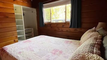 Un dormitorio con cama, ventilador de techo, ventana con cortinas y pared de madera.