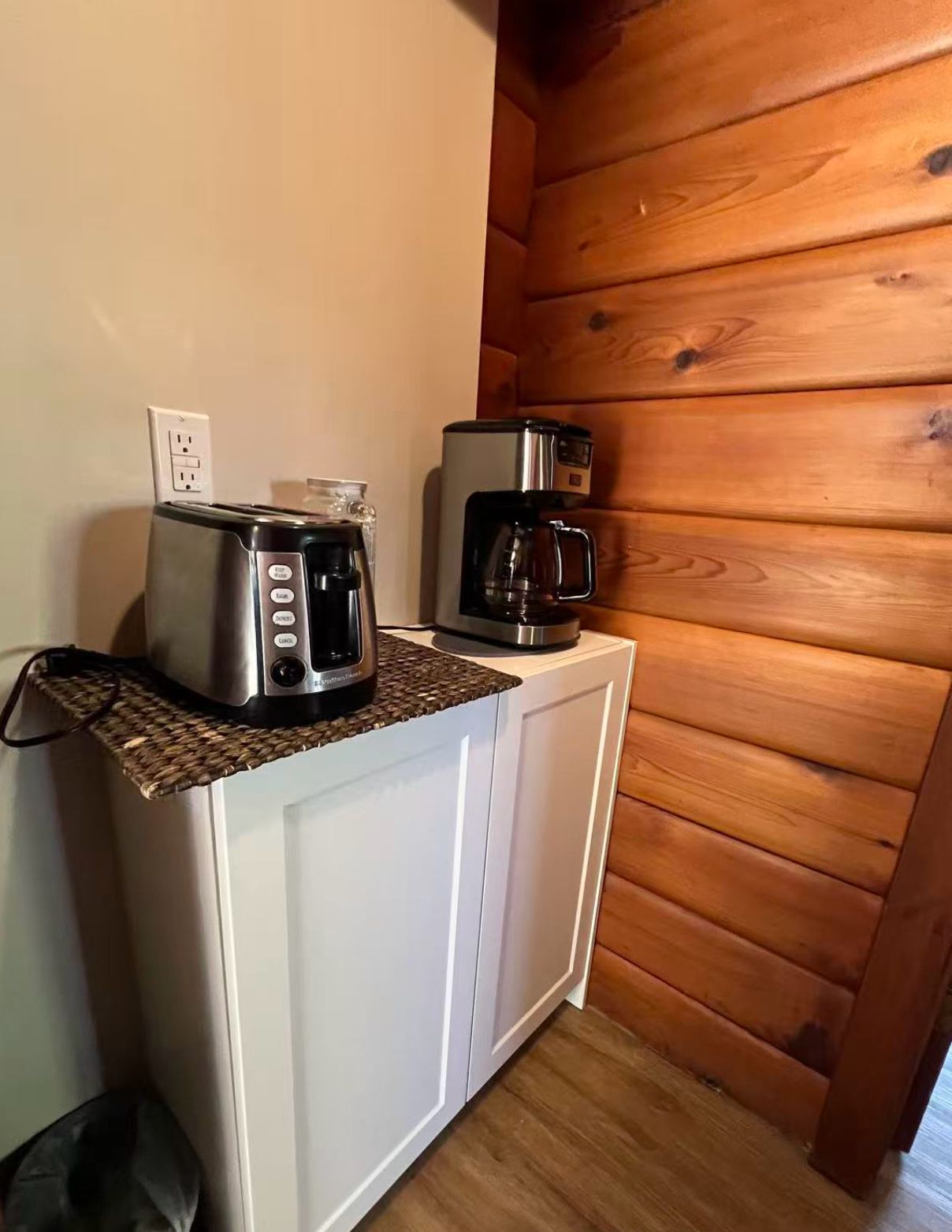 A kitchenette with a toaster, a coffee maker, and a woven mat on the countertop.