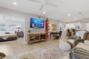 A modern living room with a flat-screen TV, a dining area with a table and chairs, and a kitchen in the background. - Corner Condo Retreat | 1st Floor | Walk-Out Patio | Optional Saddlebrook Resort Amenities (Wesley Chapel)