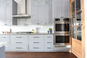 Una cocina con armarios blancos, estufa de acero inoxidable y horno doble.