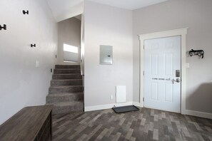 A hallway with a staircase, a white door with a sign, and a small shelf with a decorative item.