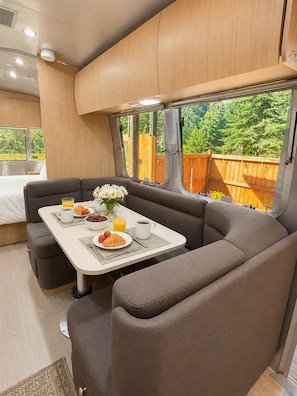 A cozy interior with a dining area, a sofa, and a window with a view of greenery. - Airstream steps to Mt. Rainier w/ covered hot tub (Ashford)