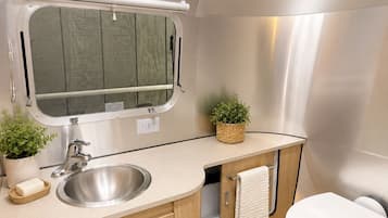 A compact RV bathroom with a sink, toilet, and a small window.
