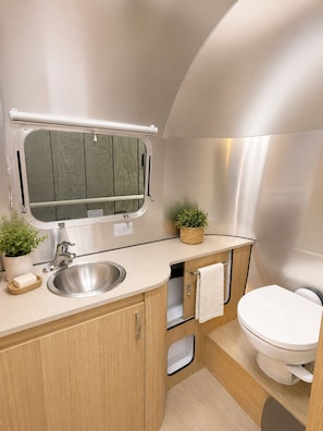 A compact RV bathroom with a sink, toilet, and a small window. - Airstream steps to Mt. Rainier w/ covered hot tub (Ashford)