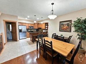 A kitchen with wooden cabinets, a stainless steel refrigerator, a microwave, and a dining area with a wooden table and chairs. - Ski-In/Ski-Out / Private Hot Tub & Mountain Views (Kimberley)
