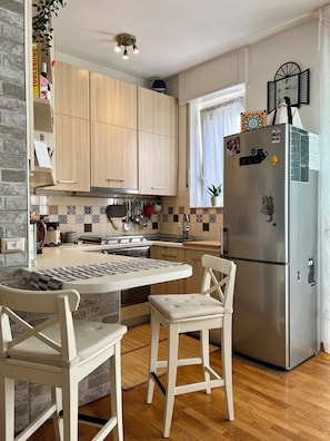 A modern kitchen with wooden cabinets, a stainless steel refrigerator, and a dining area with a table and chairs. - Nido Milano | La tua casa lontano da casa (Milano)
