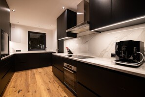 Una cocina moderna con armarios oscuros, encimera de mármol y cafetera integrada.