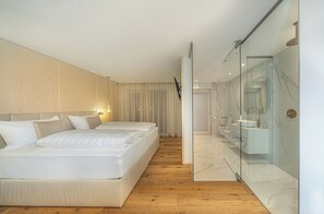 Habitación de hotel moderna con una cama grande, un baño con paredes de vidrio y suelo de madera.