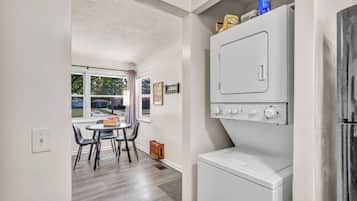 A laundry room with a washer and dryer, a table with chairs, and a window with a view of the outside.