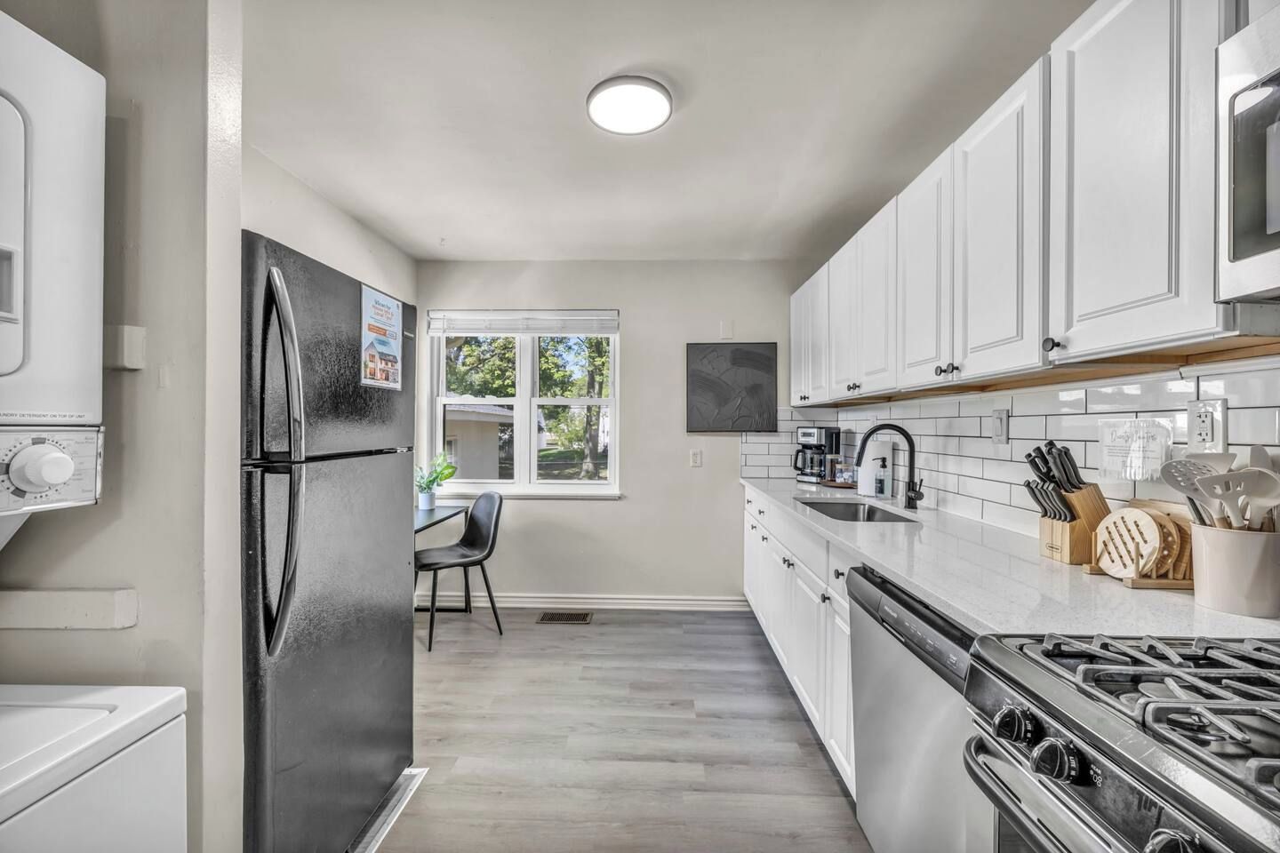 Una cocina moderna con armarios blancos, un refrigerador de acero inoxidable, una estufa a gas y un ventanal que proporciona luz natural.