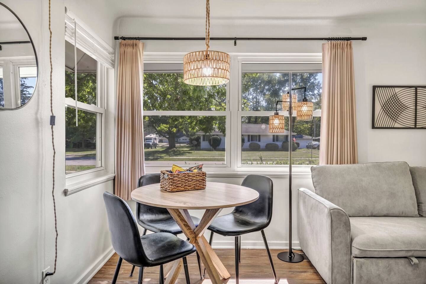 A room with a round table, two chairs, a sofa, and a large window with curtains.