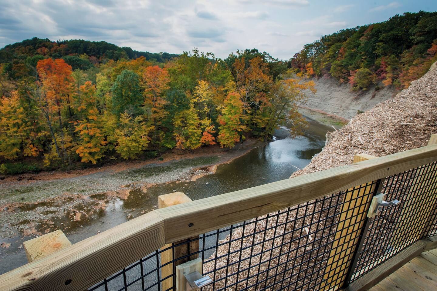A river with autumn foliage, a wooden bridge, and a metal railing.