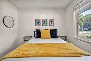 Un dormitorio con una cama, una ventana y tres cuadros abstractos en la pared.