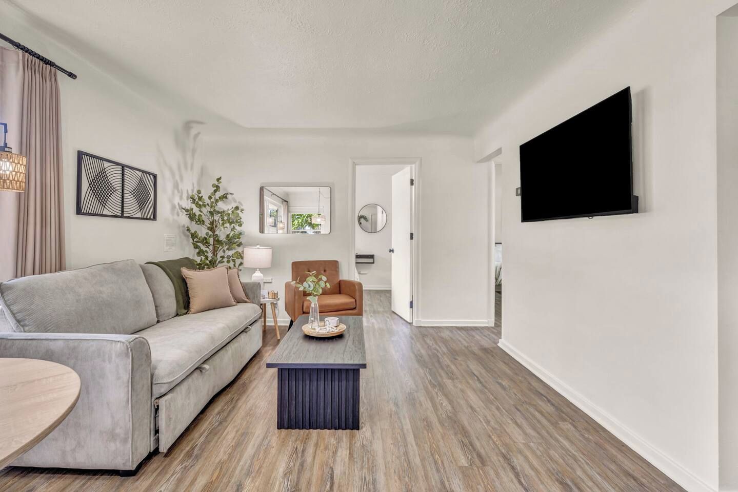 A modern living room with a grey sofa, a brown armchair, a coffee table, and a flat-screen TV mounted on the wall.
