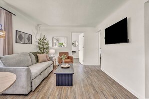 Ein modernes Wohnzimmer mit einem grauen Sofa, einem braunen Sessel, einem Couchtisch und einem wandmontierten Flachbildfernseher.