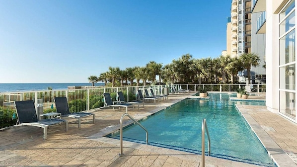 Ein Poolbereich mit Liegestühlen und Blick auf das Meer.