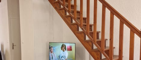 A living room with a wooden staircase, a television on a wooden stand, and a white coffee table.