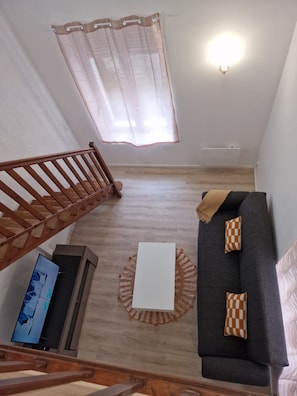 A living room with a staircase, a sofa, a coffee table, and a television.